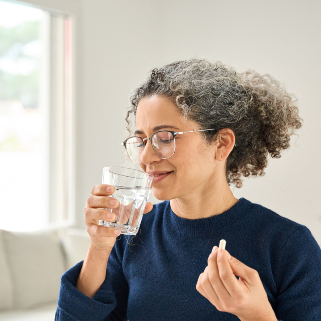 Woman holding a glass of water and a pill in a bright room