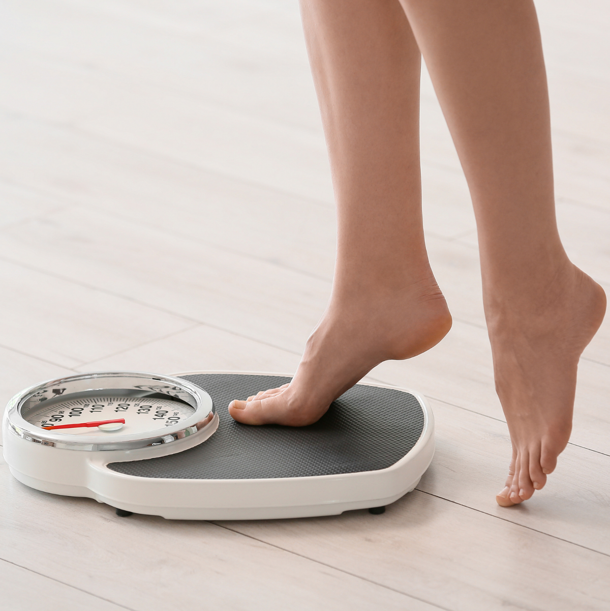 Person stepping onto a digital bathroom scale on a light wooden floor.